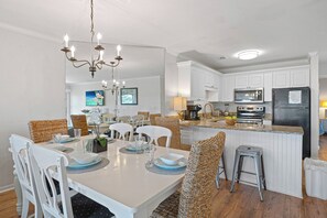 A modern kitchen with white cabinetry, a central island, and a dining area with white chairs and a chandelier.