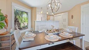 A dining area with a large table set for four, white chairs, and a chandelier. - Oceanfront Sea Cloisters Family 3BR Villa • Private Stairs to Beach, Pool & Boardwalk (Hilton Head Island)