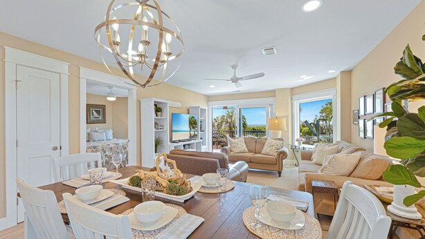 A dining area with a wooden table set for a meal, a ceiling fan, and a view of the outdoors. - Oceanfront Sea Cloisters Family 3BR Villa • Private Stairs to Beach, Pool & Boardwalk (Hilton Head Island)