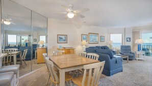 A modern living room with a wooden dining table, blue patterned sofa, and a ceiling fan. - Beachfront Sea Cloisters Villa w Ocean Views, Balcony & Complex Pool (Hilton Head Island)