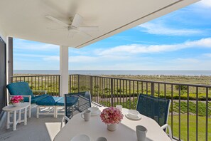 A balcony with a table, chairs, and a view of the ocean.