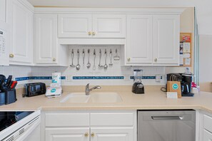 A modern kitchen with white cabinetry, a built-in sink, a coffee maker, and various utensils hanging above the counter.