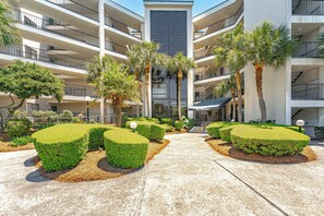 A multi-story hotel with a central courtyard featuring neatly trimmed hedges and palm trees.
