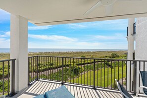 A balcony with a view of the ocean and a landscaped area.
