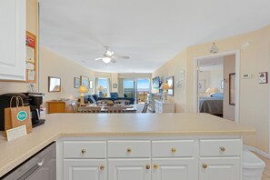 A hotel room with a kitchenette, a dining area, a living room with a sofa and a coffee table, and a view of the ocean.