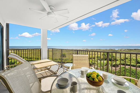 A balcony with a table, chairs, and a bowl of fruit.