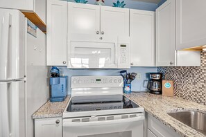 Una cocina con armarios blancos, microondas, cafetera y estufa.