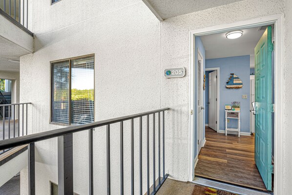 Edificio residencial con balcón, puerta con placa de número y escalera que conduce a un piso superior.