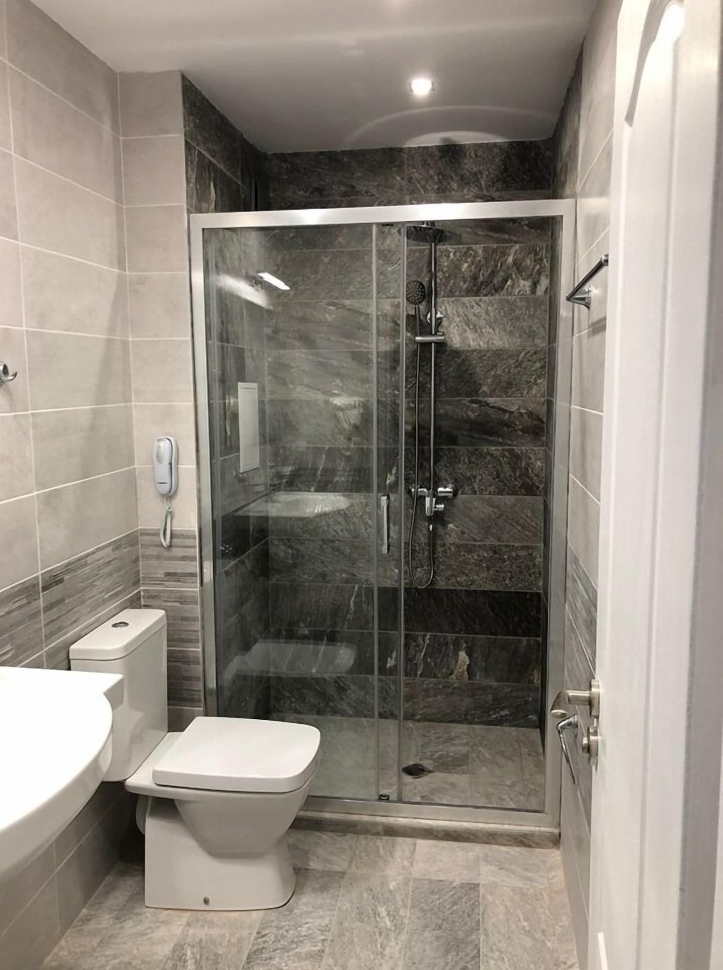 A modern bathroom with a glass-enclosed shower, a toilet, and a sink.