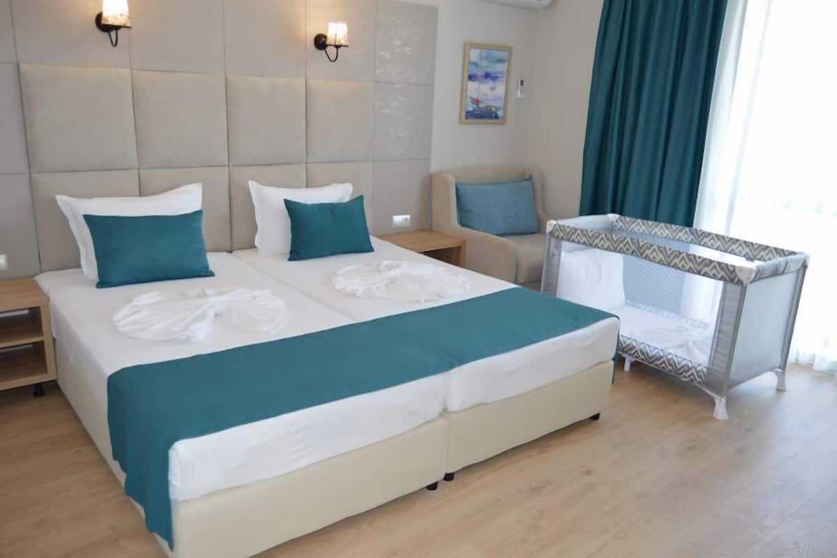 A hotel room with a large bed, a small sofa, a crib, and two wall-mounted lights.