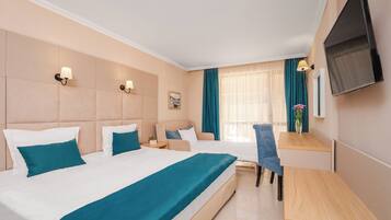A hotel room with two beds, a desk, a chair, a TV, and a window with curtains.