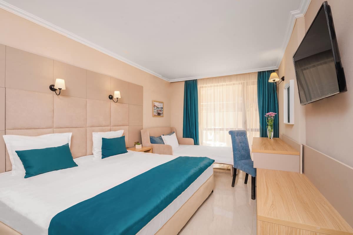 A hotel room with two beds, a desk, a chair, a TV, and a window with curtains.