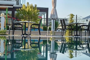 Un espace extérieur avec une piscine, des chaises et des tables, entouré d’une clôture en métal et de verdure.