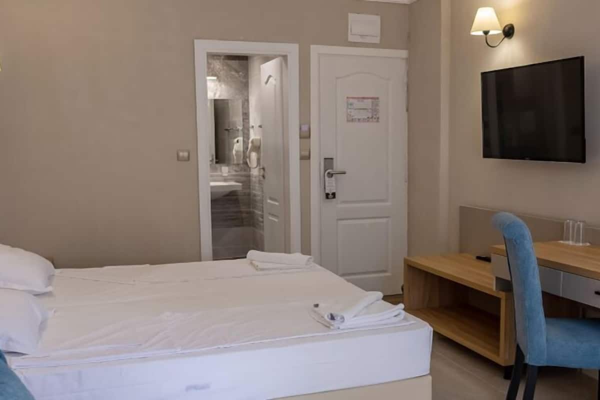 A hotel room with a bed, a desk, a chair, a TV, and a door.