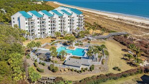 Ein mehrstöckiges Hotel mit Pool, umgeben von einer begrünten Anlage mit Palmen und Blick auf den Strand.