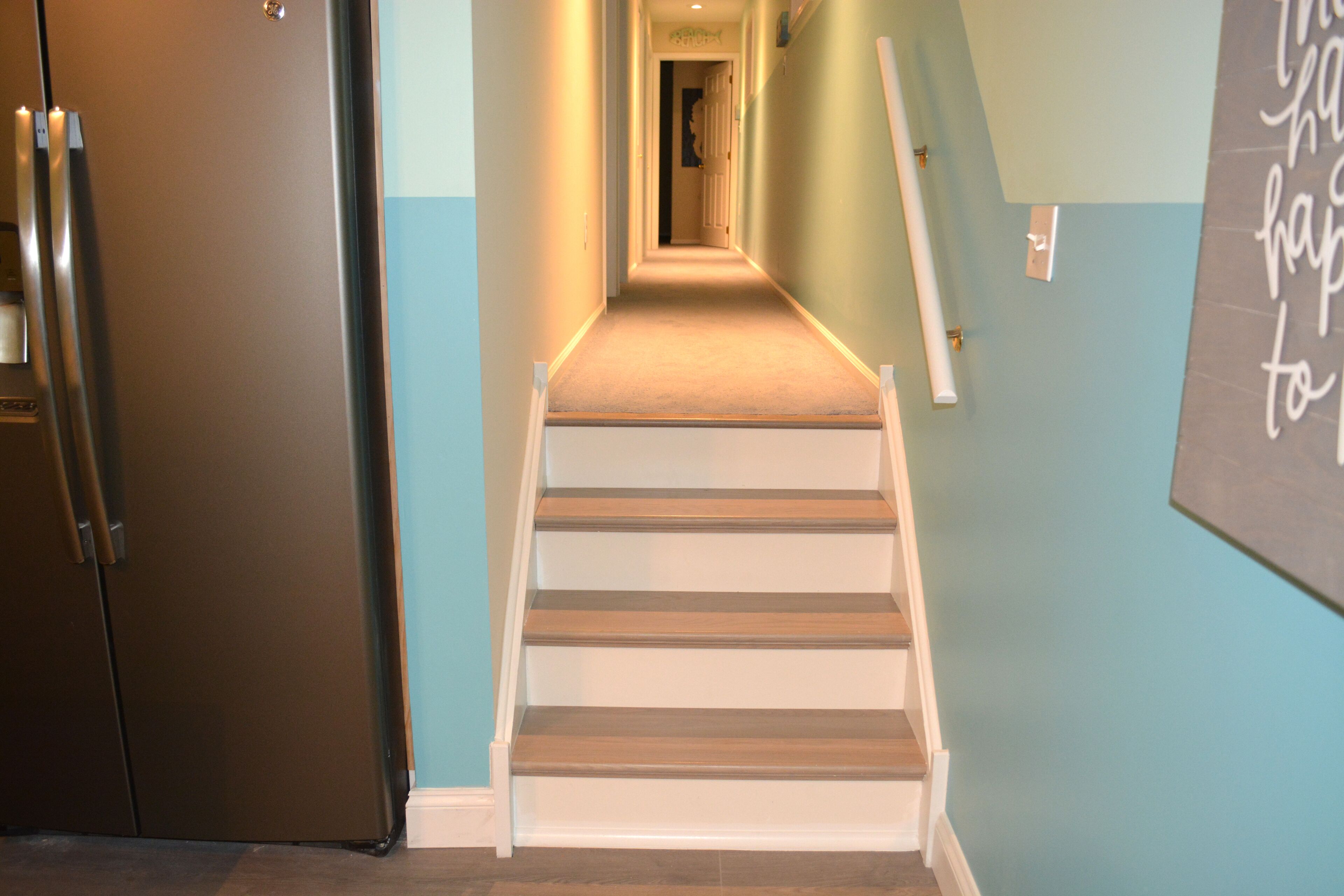 Ein Flur mit einer Holztreppe, einem Kühlschrank und einer Tafel an der Wand.