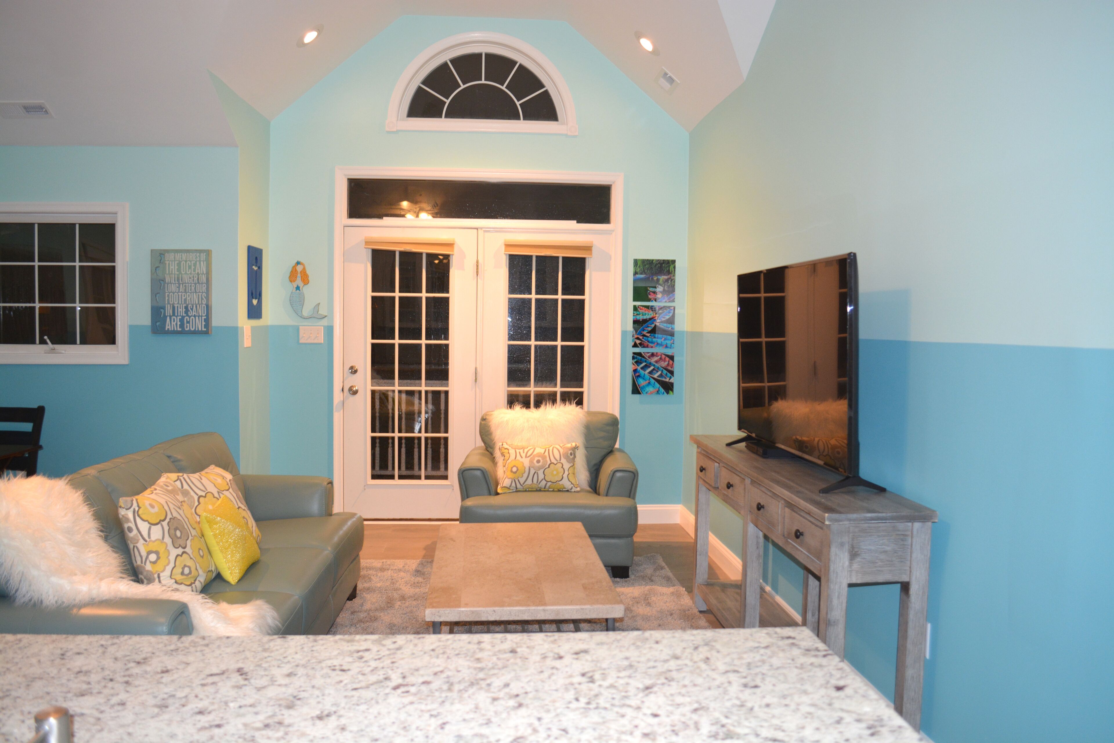 A living room with a blue wall, a large window, a sofa, a coffee table, and a television.