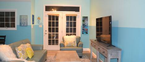 A living room with a blue wall, a large window, a sofa, a coffee table, and a television.