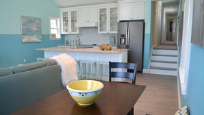A modern kitchen with white cabinets, a stainless steel refrigerator, and a dining area with a wooden table and a yellow bowl. - Sleeps 10 - 3 bedroom, 2 bath, beach chairs, tags, very close to beach/boardwalk (Ocean City)