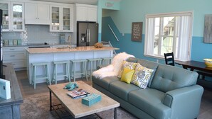 A modern kitchen with white cabinets, a central island with bar stools, and a teal-colored sofa with decorative pillows. - Sleeps 10 - 3 bedroom, 2 bath, beach chairs, tags, very close to beach/boardwalk (Ocean City)