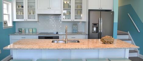 A kitchen with white cabinets, a stainless steel refrigerator, a granite countertop, and four light blue bar stools.