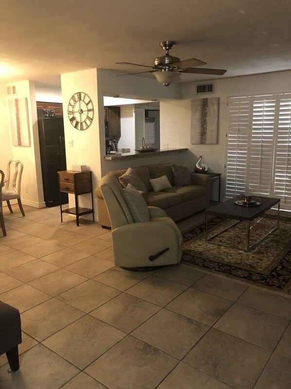 Un salon avec un canapé, une table basse, une horloge et un ventilateur de plafond.