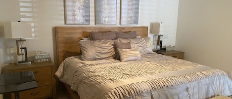 A neatly arranged bedroom with a wooden headboard, a large bed with multiple pillows, bedside tables with lamps, and a bench at the foot of the bed.