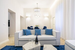A modern living room with a sofa, two side tables, a chandelier, and a large mirror.