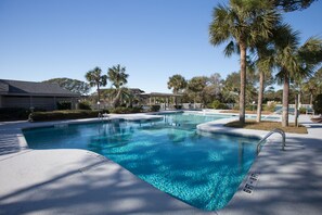 Une piscine à l’eau d’un bleu cristallin, entourée de palmiers et dotée d’un espace abrité.