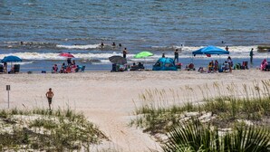 Une plage où des gens se détendent sous des parasols, certains dans l’eau et d’autres sur le sable.