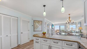 A spacious kitchen with white cabinetry, granite countertops, and a central island. There are pendant lights and a chandelier above the island.