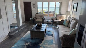 Una sala de estar acogedora con un ventanal grande, muebles de mimbre y un tapete azul con estampado floral.