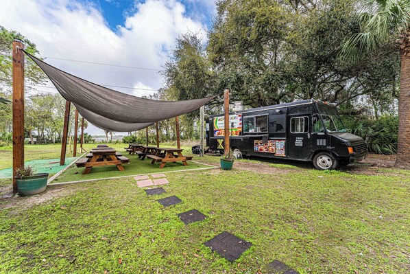 Camión de comida estacionado junto a un área de picnic con toldo, mesas y un campo de césped.