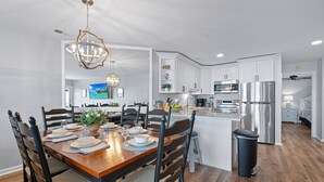 Una cocina moderna con armarios blancos, electrodomésticos de acero inoxidable y un comedor con mesa y sillas de madera.