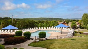 Une piscine entourée d’une clôture et de verdure, avec des chaises longues et des parasols.