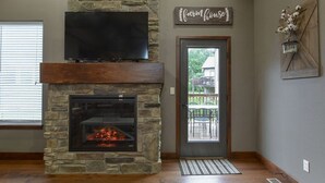 Une cheminée en pierre avec un téléviseur au-dessus, une porte ornée d’une plaque indiquant « ferme », et une vue sur un balcon à l’extérieur.