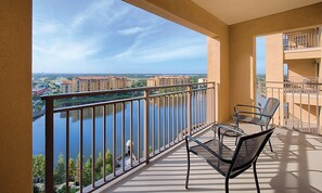 A balcony with a view of a river and buildings, featuring a chair and a small table. - Rare Find! 3 BR Dlx Sleeps 10 -Bonnet Creek Resort-5 Pools & More (Orlando)