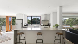 Cozinha moderna com ilha central, três banquetas, uma janela grande e vista para o verde lá fora.