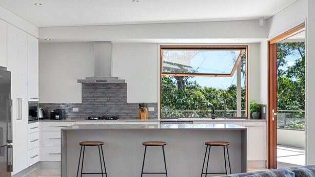 Una cucina moderna con un'isola grande, sgabelli da bar e vista su del verde attraverso un'ampia finestra.