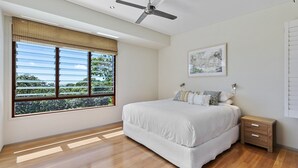 Una camera da letto con un letto grande, una ventola a soffitto, un comodino e una finestra con persiane.