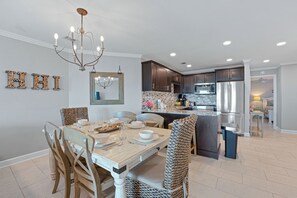 A modern kitchen with dark cabinetry, a central island, and a dining area with a wooden table and chairs.