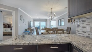 A modern kitchen with a marble island, dark cabinetry, and a dining area with a view.