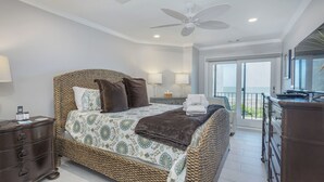 A spacious bedroom with a large bed, a ceiling fan, and a balcony with a view.