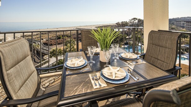 A dining table set with plates, cutlery, and glasses, overlooking a beach and pool area.