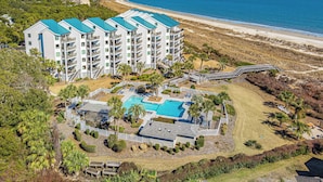 Un hôtel à plusieurs étages doté d’une piscine, entouré d’un espace paysager agrémenté de palmiers et offrant une vue sur la plage.
