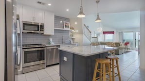 A modern kitchen with stainless steel appliances, a large island with stools, and a view to a balcony.