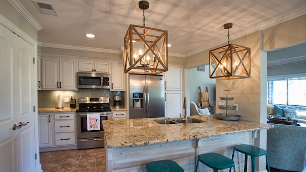 A modern kitchen with white cabinetry, stainless steel appliances, a granite countertop, and teal bar stools. - Hilton Head Villa: 2 King Suites, Loft, Updated Interiors & Beach Perks (Hilton Head Island)