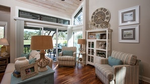A spacious living room with a large window, a ceiling fan, and a decorative clock. - Hilton Head Villa: 2 King Suites, Loft, Updated Interiors & Beach Perks (Hilton Head Island)