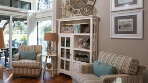 A cozy living room with striped sofas, a wooden cabinet with glass doors, and a large wall clock. - Hilton Head Villa: 2 King Suites, Loft, Updated Interiors & Beach Perks (Hilton Head Island)