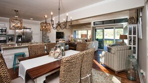 A spacious living area with a dining table, wicker chairs, a chandelier, and a view of the outdoors. - Hilton Head Villa: 2 King Suites, Loft, Updated Interiors & Beach Perks (Hilton Head Island)
